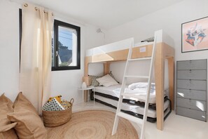 Une chambre avec un lit superposé, une fenêtre, un bureau, une chaise, un panier et un classeur gris.