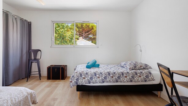 Um quarto com cama, janela com vista, uma cadeira e uma mala.