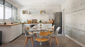 Cozinha moderna com mesa de jantar para seis pessoas, armários brancos, uma janela grande e uma geladeira.