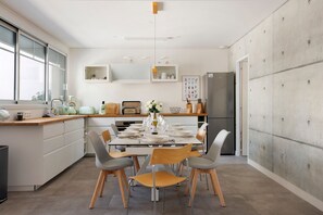 Eine moderne Küche mit Esstisch für sechs Personen, weißen Schränken, einem großen Fenster und einem Kühlschrank.