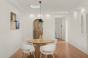 A dining area with a round wooden table, white chairs, a pendant light, and a view into the kitchen. - César’s Oasis – Manrique-Style Architecture Near Playa de las Cucharas (Costa Teguise)