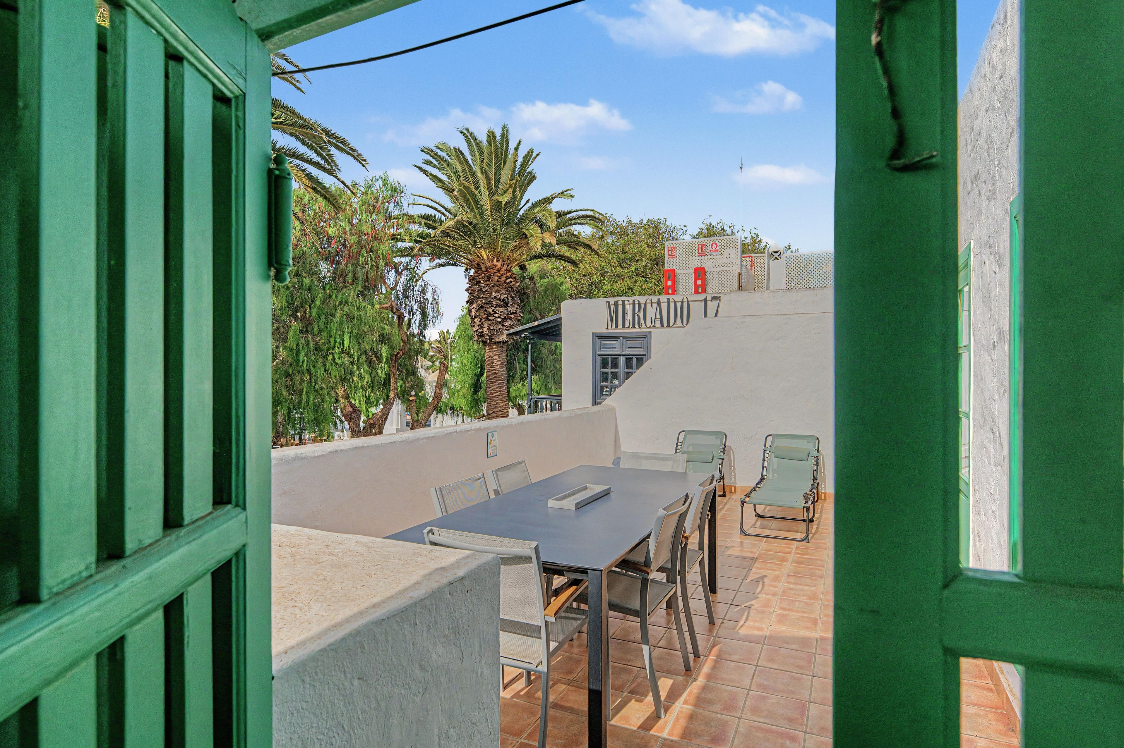 Eine Außenpatio mit Tisch und Stühlen, Blick auf eine Palme und ein Gebäude mit dem Schild 'MERCADO 17'.