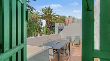 Eine Außenpatio mit Tisch und Stühlen, Blick auf eine Palme und ein Gebäude mit dem Schild 'MERCADO 17'.
