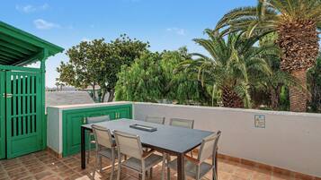 An outdoor patio with a table and chairs, surrounded by greenery and palm trees.
