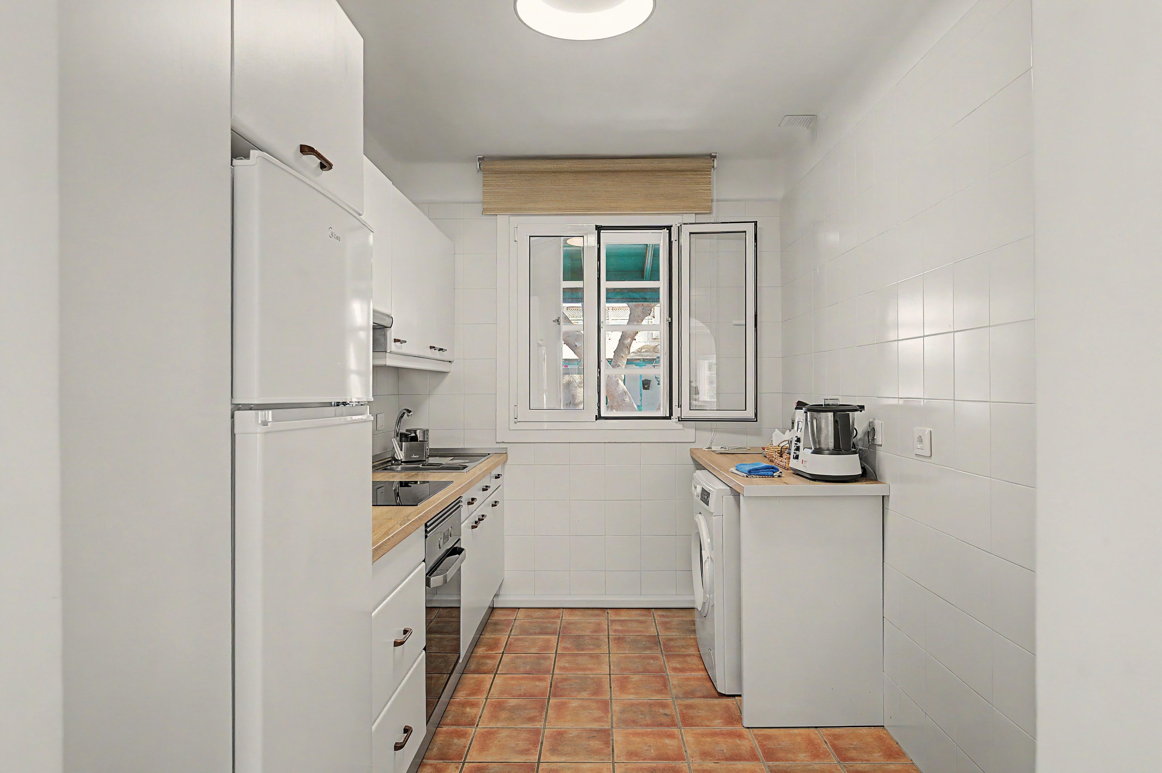 Eine kompakte Küche mit weißen Schränken, einem eingebauten Backofen, einem Spülbecken und einem kleinen Fenster mit Blick.