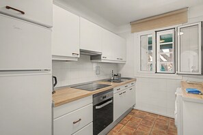 A compact kitchen with white cabinetry, a black oven, a wooden countertop, and a window with a view.