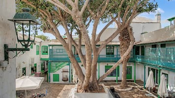 A courtyard with a large tree, a staircase, and buildings with green accents.