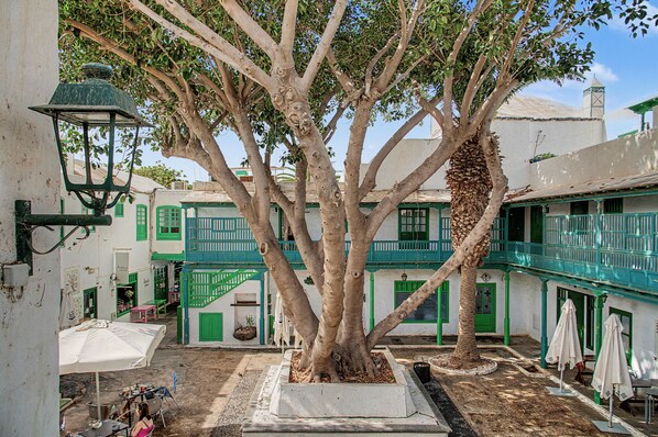 A courtyard with a large tree, a staircase, and buildings with green accents.