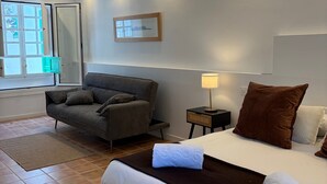 Ein Hotelzimmer mit Bett, Sofa, Nachttisch, Lampe, Fenster mit Blick und einem Bild in einem Rahmen an der Wand.