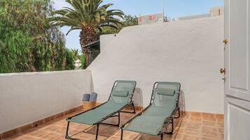 Un balcón con dos sillones verdes, una pared blanca y una palmera.