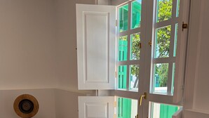 Ein Zimmer mit einem schwarzen Ledersessel, einem kleinen Holztisch mit einem Lautsprecher und einem Fenster mit grünen Fensterläden.