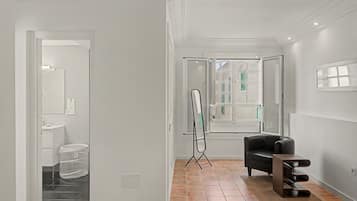 A modern interior with a black leather chair, a standing mirror, and a view of a bathroom through a glass door.