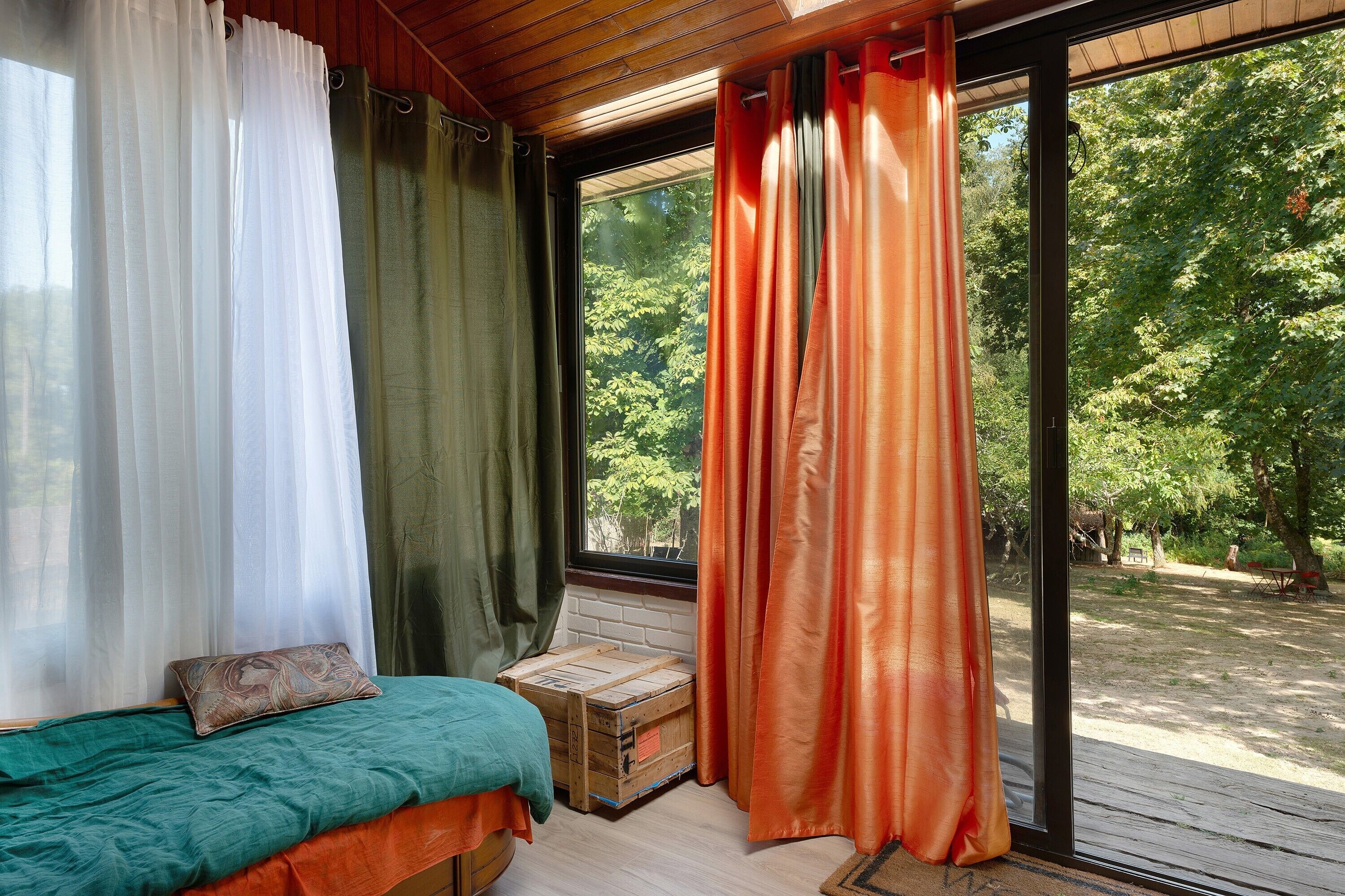 A room with a bed, a window with curtains, and a view of a garden.