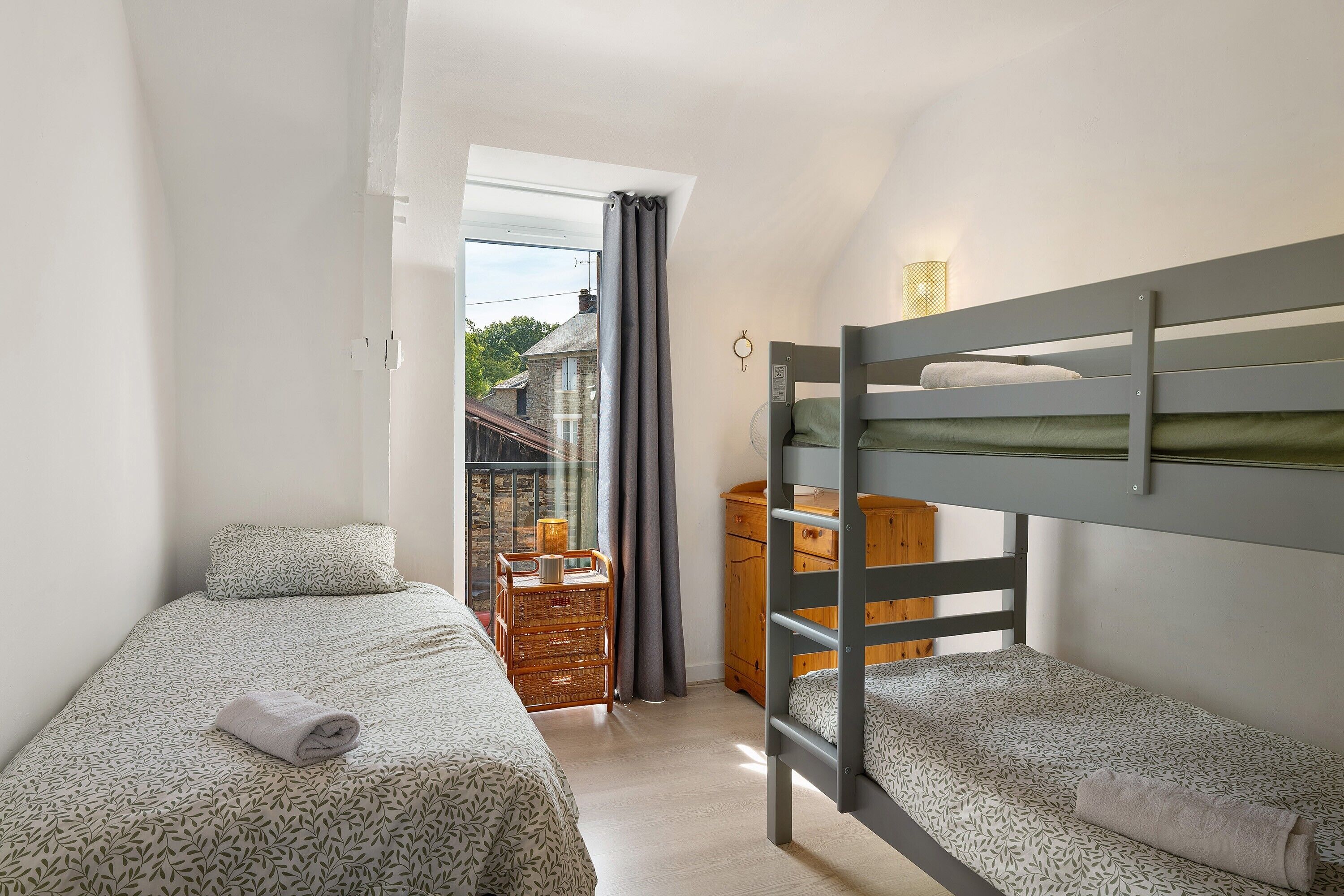 Una habitación pequeña con dos camas individuales, un aparador de madera y una mesita con una lámpara.
