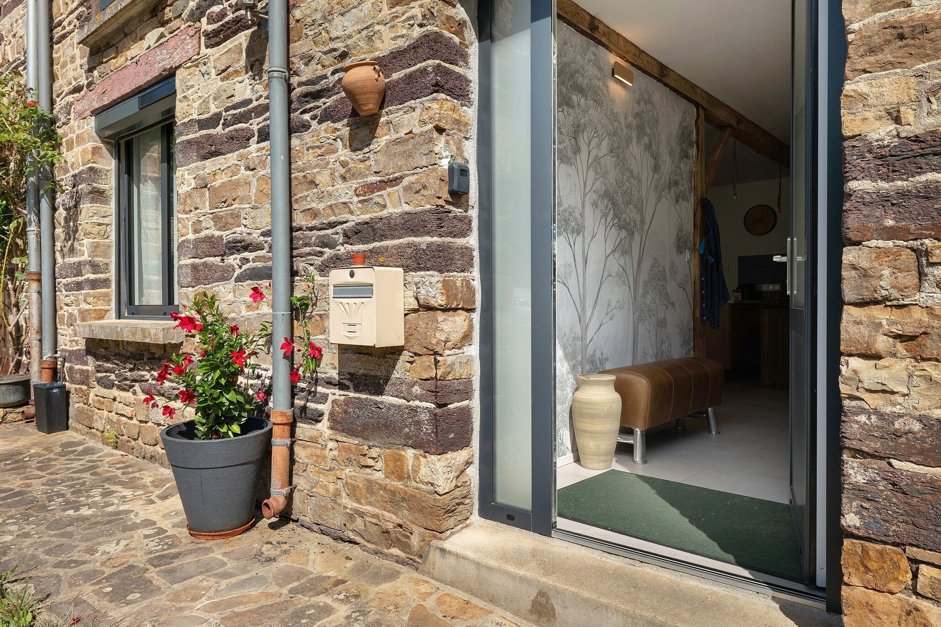 A stone building with a door leading to a room with a bench and a wall-mounted clock.