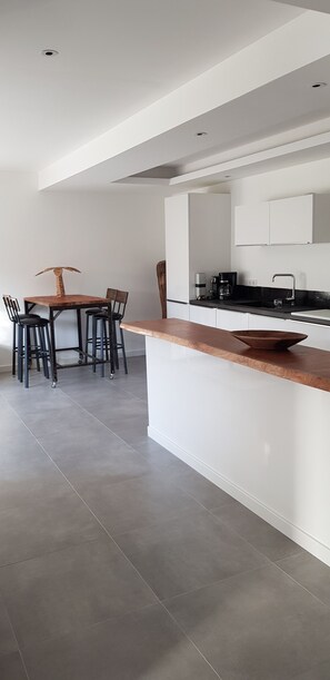 A modern kitchen with a central island, a dining area with chairs, and a coffee machine. - Garden-Level Apartment (Sainte-Maxime)
