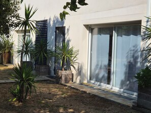 A modern building with a paved courtyard, large potted plants, and a sliding glass door. - Garden-Level Apartment (Sainte-Maxime)