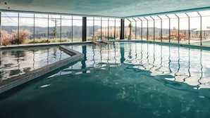 Piscina interior com paredes de vidro transparente e vista para montanhas.