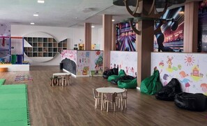 Zona infantil con mesas, sillas, pufs y murales coloridos.
