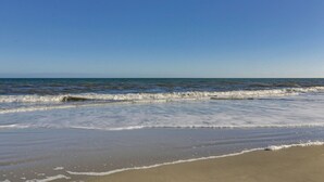 A beach with waves gently lapping onto the shore under a clear blue sky. - Sunset Rentals | Island Club 6102 (Hilton Head Island)