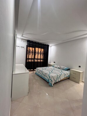 Un dormitorio con una cama, una mesita de noche, un armario y una puerta con cortina.
