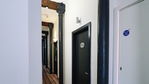 Um corredor de hotel com portas pretas, carpete listrado e placa de porta corta-fogo.