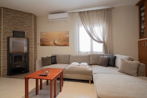 A living room with a sofa, a coffee table, a fireplace, and a painting on the wall. - Venetia Beach House by Rentals Pro - Mouries Halkidiki (Mouries)