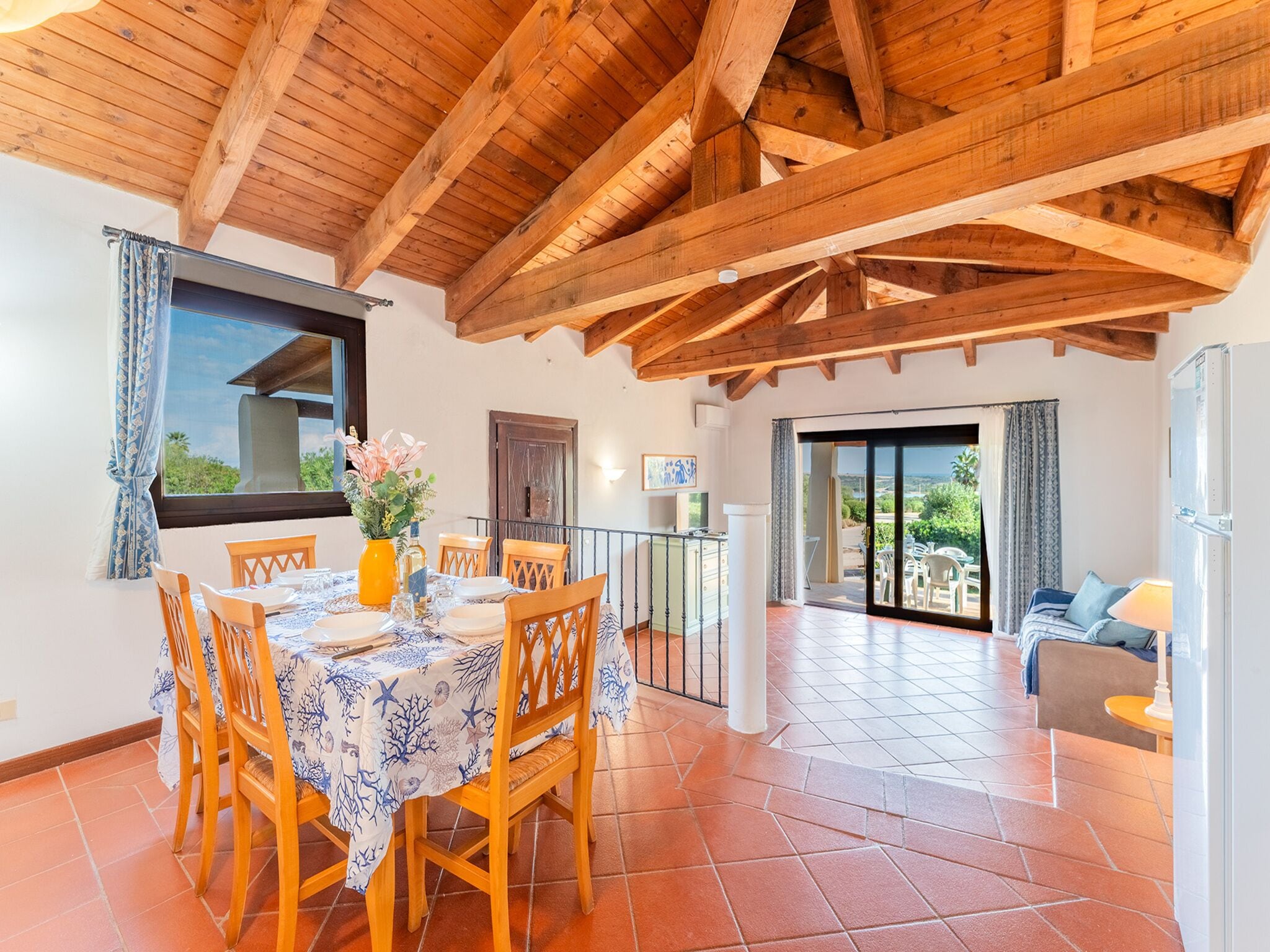 Uma sala de jantar com teto de madeira, uma mesa posta para quatro pessoas e vista para o exterior através de uma porta deslizante.