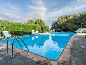 Ein rechteckiger Pool mit Steinrand, umgeben von weißen Liegestühlen und einer Hecke.