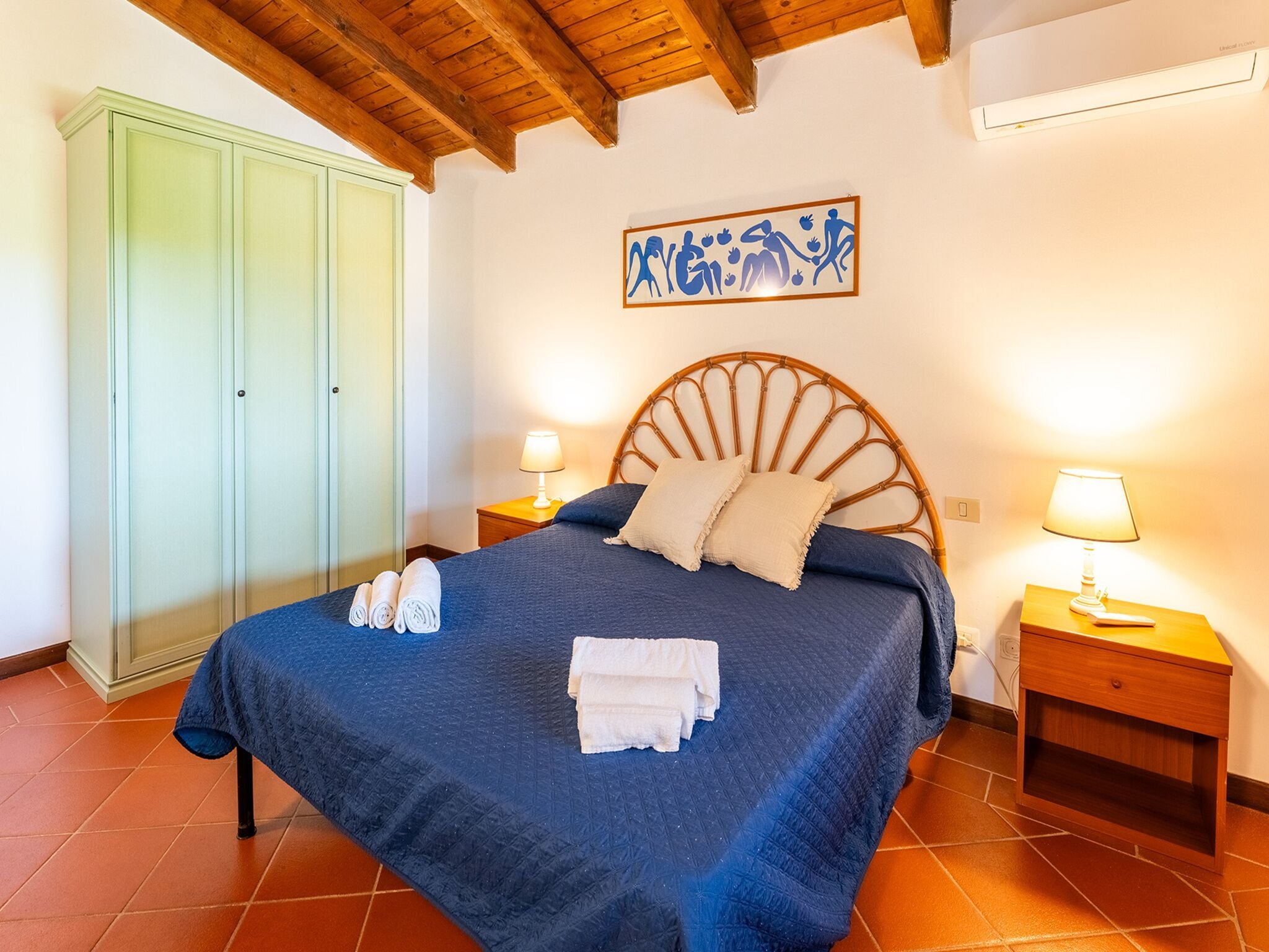 A bedroom with a bed, two bedside tables with lamps, a wardrobe, and a wall decoration.