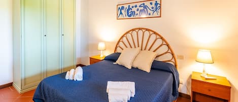 Un dormitorio con una cama, dos mesitas de noche con lámparas, un armario y un adorno en la pared.