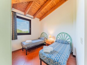 Ein Zimmer mit zwei Betten, einem Vorhangfenster, einer Holzbalkendecke und einem gefliesten Boden.