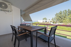 A balcony with a table and chairs, overlooking a landscaped garden and a building. - Sea Whisper by RentalsPro - Pefkohori Halkidiki (Pefkohori)