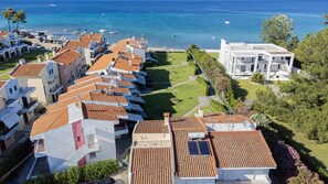 A coastal residential area with terracotta-tiled houses, a modern building, and a marina with boats. - Sea Whisper by RentalsPro - Pefkohori Halkidiki (Pefkohori)