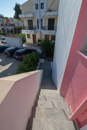 Ein Wohngebäude mit einer schmalen Treppe zu einer Tür, parkenden Autos und blauem Himmel.