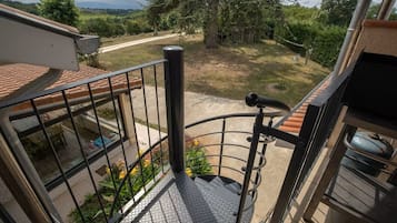 Un balcon avec une balustrade en métal, un escalier en métal et une vue sur un jardin et une route.