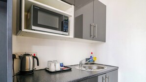 Eine kompakte Küchenzeile mit Mikrowelle, Wasserkocher, Kaffeemaschine und Spüle mit einer Flasche Geschirrspülmittel.