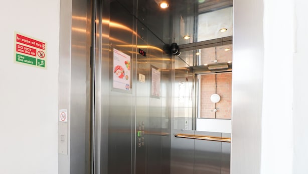 An elevator with a digital display, emergency instructions, and a glass door. - Apartment 610 (Nottingham)