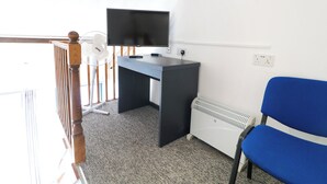 A room with a desk, a television, a blue chair, a radiator, and a wooden staircase railing. - Apartment 610 (Nottingham)