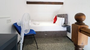 A small, neatly arranged room with a bed, a chair, a desk, and a standing fan. - Apartment 610 (Nottingham)
