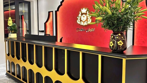 A reception desk with a red and gold color scheme, a logo, and a potted plant. - Dollar Hotel An Khanh (Hanoi)