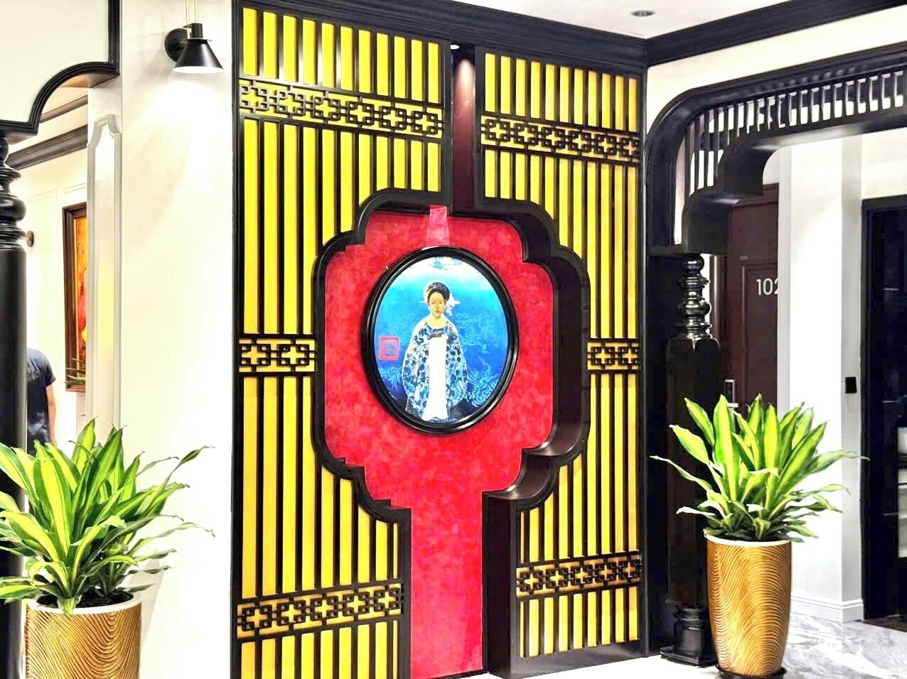 A traditional Chinese-style entrance with a red door, a framed portrait, and potted plants.