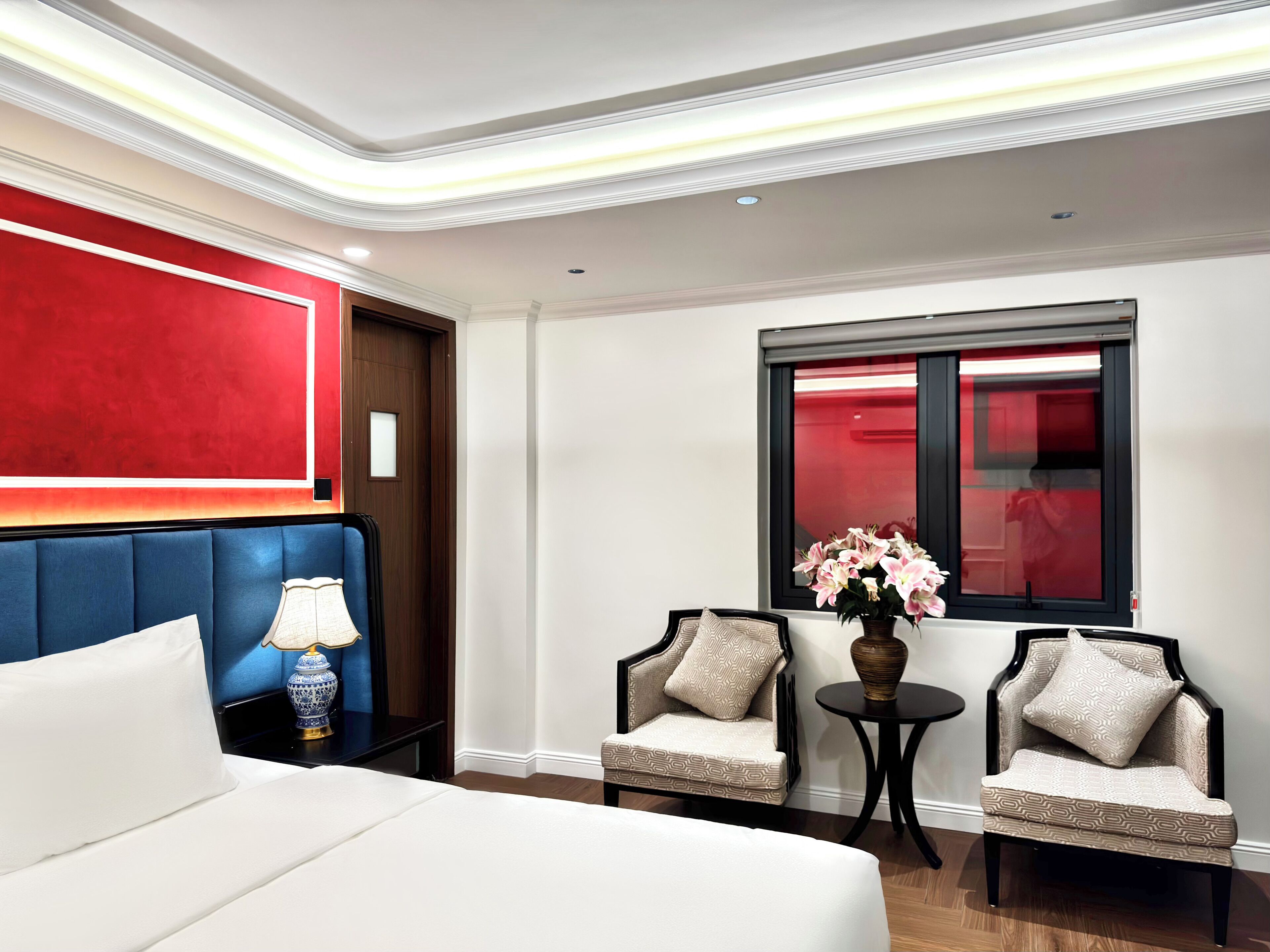 A hotel room with a large bed, two armchairs, a small table, and a window with a view of a red building.