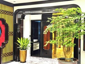 A modern entrance with a large potted plant, a decorative wall, and a number '102' sign. - Dollar Hotel An Khanh (Hanoi)