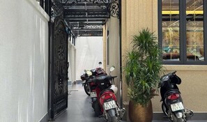Un pasillo estrecho con dos motocicletas estacionadas a la derecha, una planta en maceta y un portón decorativo en la entrada.