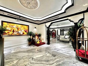 A lobby with a marble floor, a large floral painting, a reception desk, and a seating area with a sofa and armchairs.