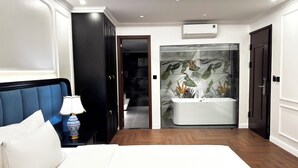 A modern bedroom with a large bed, a nightstand, a lamp, a dark wardrobe, a bathroom with a bathtub and a shower, and a ceiling with recessed lighting. - Dollar Hotel An Khanh (Hanoi)
