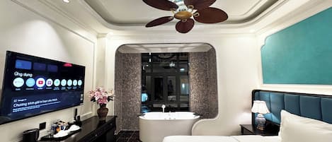 A hotel room with a bed, a TV displaying streaming services, a ceiling fan, and a bathroom with a bathtub and shower.