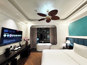 A hotel room with a bed, a TV displaying streaming services, a ceiling fan, and a bathroom with a bathtub and shower.