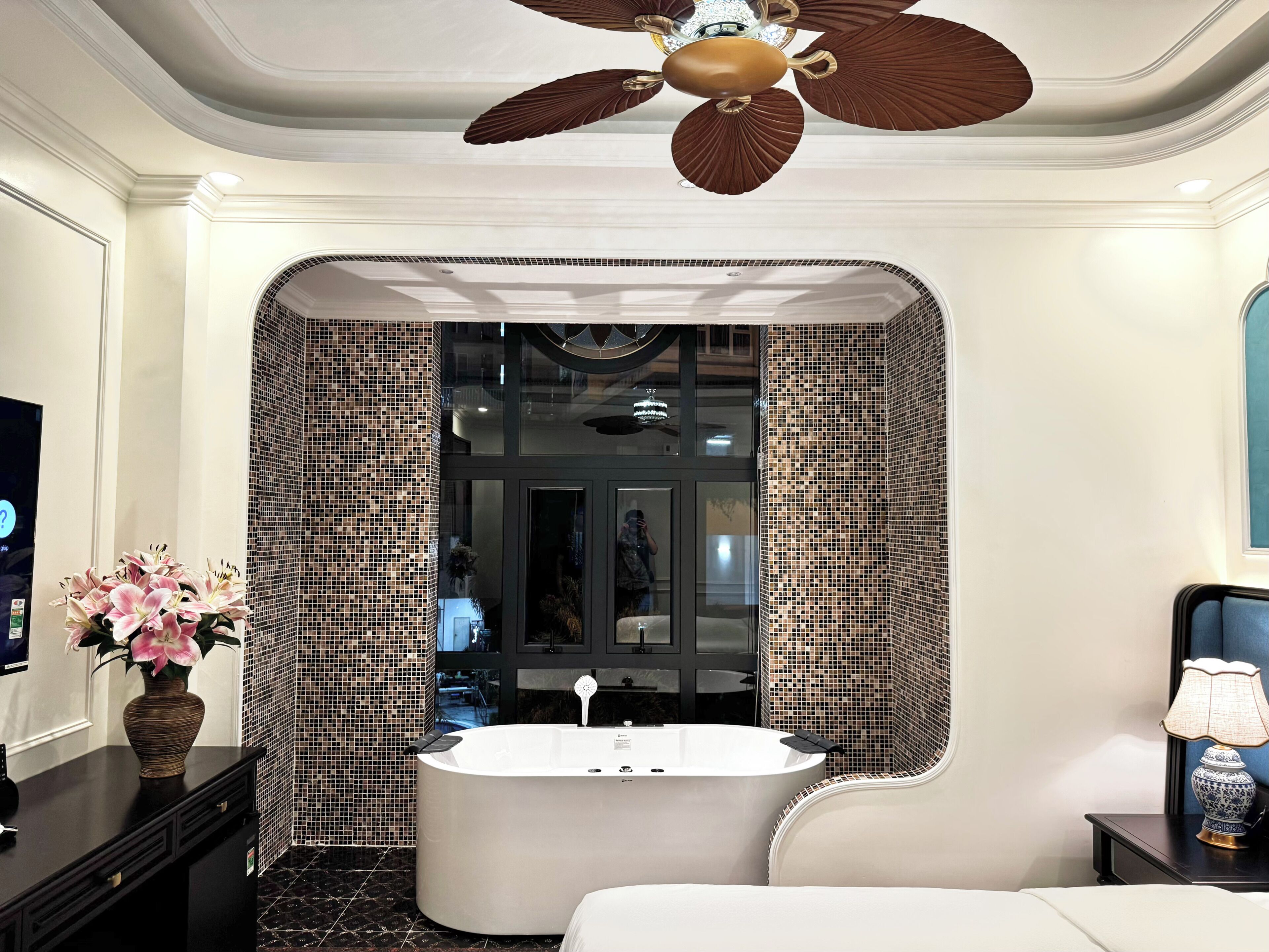 Une salle de bain moderne avec une baignoire sur pieds, un ventilateur de plafond et un vase décoratif posé sur le meuble-lavabo.